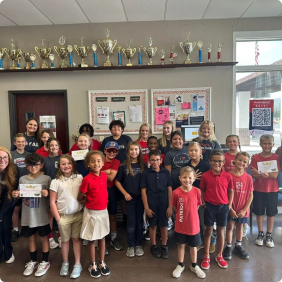 Group of elementary students standing together in a classroom smiling at the camera